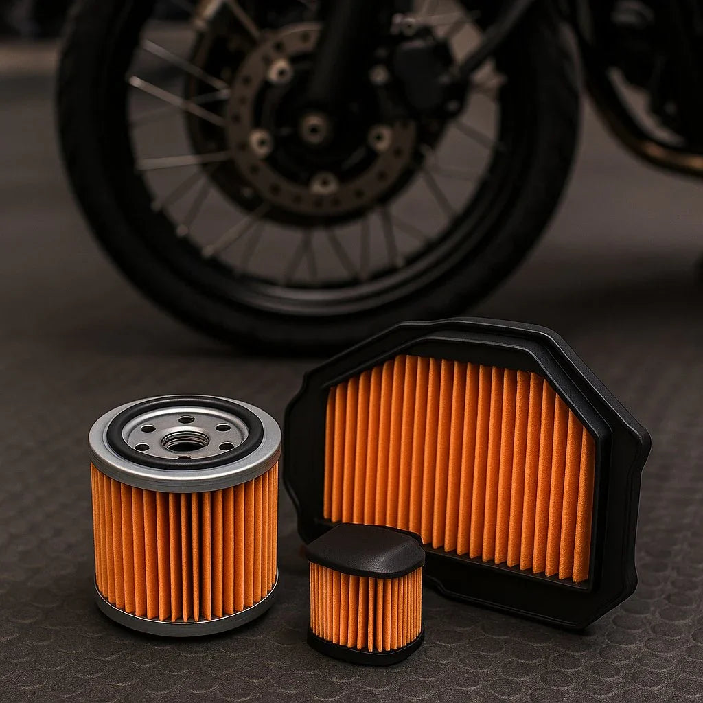Motorcycle air and oil filters with orange pleats on textured surface, bike wheel in background